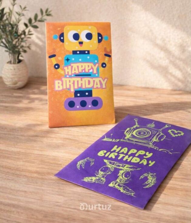Product cover for the Robot Printable Gift Envelope Bundle by Nurtuz. Shows two assembled envelopes on a wooden table: one orange with a friendly yellow robot and one purple with a mechanical bot design, both featuring "Happy Birthday" text.