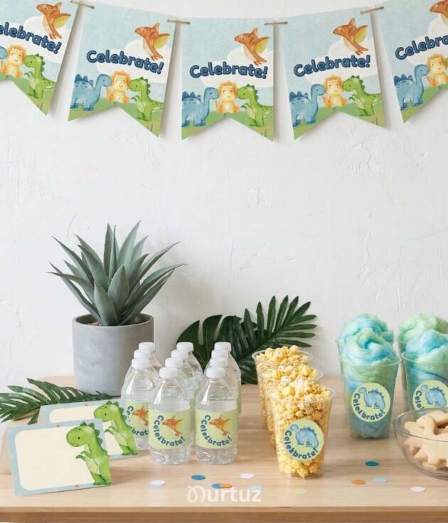 Product cover for the Baby Dinosaur Printable Party Set by Nurtuz. Features a styled dessert table with dinosaur-themed banners, water bottle labels, popcorn cups with stickers, and dinosaur cookies in a soft blue, green, and orange palette.