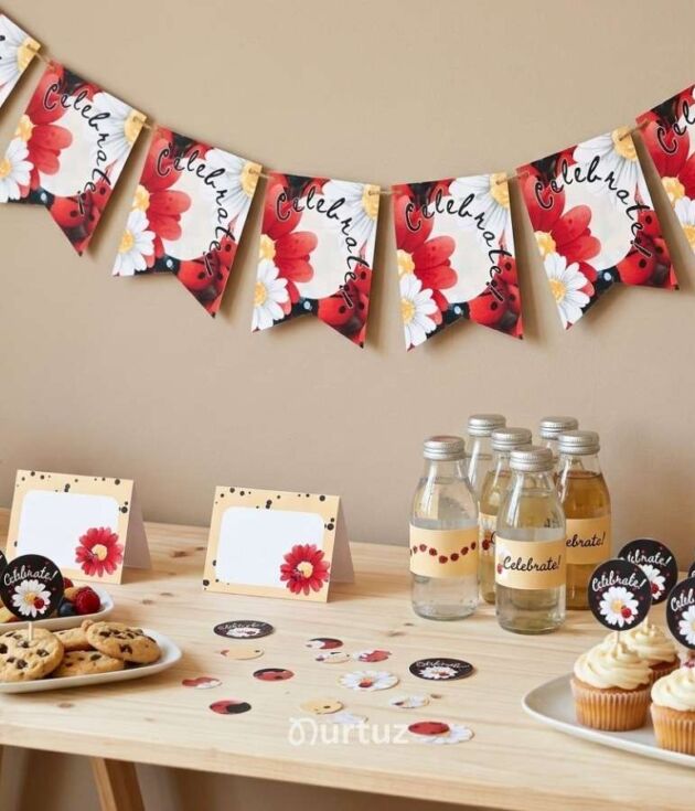 Mockup cover image of the Ladybug Printable Party Set by Nurtuz. Shows a wooden dessert table with cupcakes, water bottles with labels, daisy food tents, cookies, and a 'Celebrate' party banner in a red, black, and soft yellow theme.