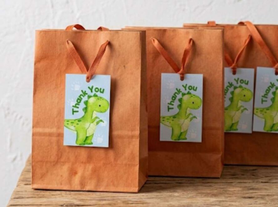 Detailed view of printable Baby Dinosaur 'Thank You' favor tags attached to rustic gift bags. Dinosaur themed tags on a textured background by Nurtuz.
